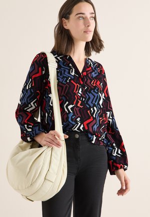Blouse multicolore à motifs variés avec manches longues, jean noir et sac hobo crème. La blouse présente des motifs en zigzag rouges, bleus et blancs.