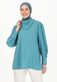 Tyrkis bluse med lange, pufærmer og knappede manchetter; glat, let stof; parret med et matchende hijab.
