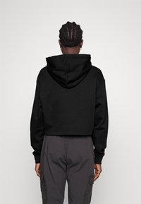 Hoodie cropped nero realizzato in morbido tessuto, con cappuccio regolabile e maniche lunghe. Il design posteriore è semplice, senza loghi o motivi visibili.