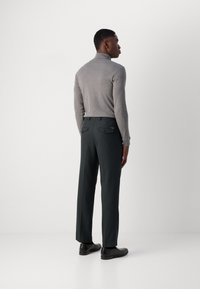 Pull en col roulé gris associé à un pantalon vert foncé. Le pantalon dispose de poches arrières, tandis que les chaussures sont noires et à texture lisse.