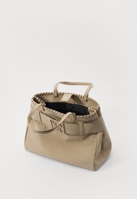 Beige leather handbag with decorative stitched rim, dual handles, and embossed logo strap. Open top reveals a dark interior lining.