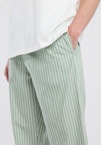 Persoon in lichtgroene broek met witte verticale strepen en een wit shirt, met de hand casual in de zak.