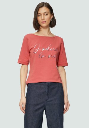 T-shirt en coton rose corail avec des manches courtes et un large décolleté. Doté d'un texte argenté brillant "J'adore la vie" sur le devant.