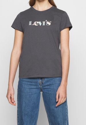 Person wearing charcoal gray Levi's t-shirt with iridescent logo and blue denim jeans, standing against a plain background.