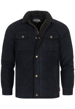 Chaqueta de pana de un azul marino oscuro con cuello de piel sintética, que presenta dos bolsillos en el pecho, botones de tono dorado y cierre frontal con cremallera.
