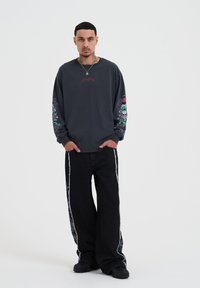 Dark gray long-sleeve shirt with colorful skull and floral graphics on sleeves, paired with black wide-leg jeans featuring side stripes.
