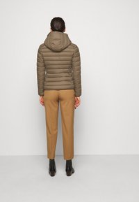 Khaki puffer-takki hupulla, tikattu pinta ja sopiva muotoilu, yhdistettynä vaaleanruskeisiin housuihin ja mustiin nilkkasaappaisiin. näkyy takaa.