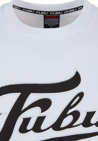 Hvit bomulls T-skjorte med en fremtredende svart brodert logo på forsiden, rund hals og teksturerte sømdetaljer.