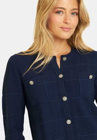 Navyblauer strukturierter Cardigan mit Rundhalsausschnitt, fünf silbernen dekorativen Knöpfen und zwei frontalen Taschen.