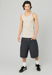 Débardeur beige à côtes, shorts en denim noir amples, chaussettes blanches et baskets noires. Palette de couleurs neutres, design décontracté et coupe relax.