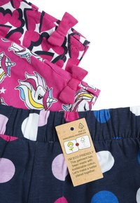Tři páry dětských šortek: růžové s jednorožci a mašlemi, bílé s černými květinami, tmavě modré s růžovými a bílými puntíky. Obsahuje ekologickou označení.