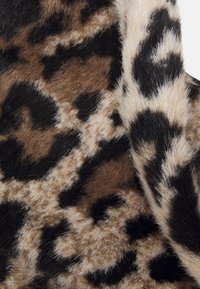 Tissu doux avec un motif léopard présentant des taches irrégulières noires et marron sur un fond beige, mettant en valeur la texture et les plis.