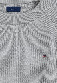 Maglione grigio a maglia con texture a coste, design a girocollo e piccolo logo ricamato sul petto con accenti rossi, bianchi e blu.