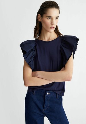 Top blu navy con maniche a sbuffo realizzato in tessuto morbido; presenta un colletto rotondo e un body aderente che si abbina a jeans scuri.