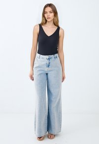 Top in riga nera con scollo a V, abbinato a jeans svasati azzurri chiari con vita alta e leggeri effetti di sbiadimento. Sandali beige completano il look.