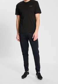 Zwarte katoenen T-shirt met korte mouwen en een klein logo, gecombineerd met smal gesneden zwarte sportbroeken en zwarte mesh hardloopschoenen.