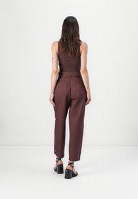 Burgundy high-waisted trousers with a tailored fit and silver button accents at the hem, paired with black heeled sandals.