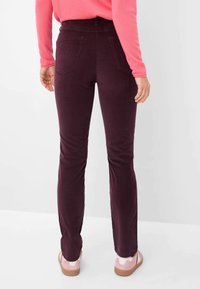 Donker bordeaux, slimfit broek met een gladde textuur, vijf zakken en een middelhoge taille. Gecombineerd met lichtroze schoenen.
