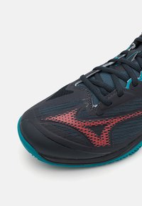 Buty sportowe z ciemnoszarym siateczkowym wierzchem, akcentami w kolorze turkusowym i czerwonymi detalami. Posiadają teksturowaną podeszwę oraz płaskie sznurowadła dla pewnego dopasowania.