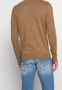 Brauner gestrickter Pullover mit langen Ärmeln, gerippten Bündchen und Saum, von hinten betrachtet. Getragen mit hellblauen Jeans.