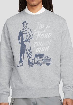 Person trägt graues Sweatshirt mit Grafik eines Mannes, der einen Schraubenschlüssel hält, und einem klassischen Truck. Der Text lautet „Ich bin ein Ford Truck Mann.“