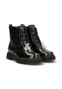 Botas de tobillo metálicas negras con una suela gruesa, que presentan un cierre con cordones en la parte delantera y un charm de oso colorido a cada lado. Textura suave, diseño minimalista.