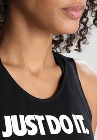 Débardeur noir avec un col ras du cou et un grand texte blanc indiquant « JUST DO IT. » Tissu lisse avec une coupe ajustée, mettant en valeur les épaules et la nuque.