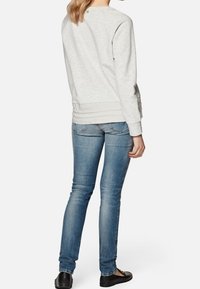 Sudadera gris claro con dobladillo y puños acanalados, combinada con jeans ajustados azules y zapatos planos negros. La vista trasera muestra un diseño de corte relajado.