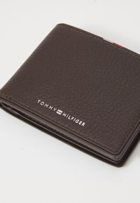 Brown leather wallet with a textured finish, featuring white "TOMMY HILFIGER" logo, and contrasting stitching along the edges.