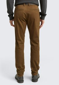 Pantaloni marrone tapered realizzati in tessuto leggero. Presentano due tasche posteriori discretamente cucite, una vita piatta e orlo chiuso.