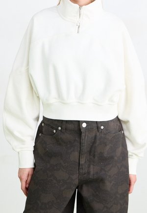 Hvid cropped sweatshirt med kvart lynlås og ballonermer, kombineret med højtaljede mørke mønstrede bukser.
