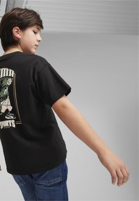 T-shirt nera in cotone a maniche corte con stampa grafica che raffigura un giocatore di basket sulla schiena. Indossata con jeans in denim blu, vista laterale.