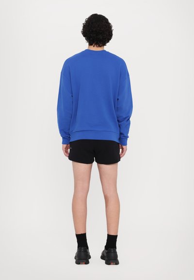 Felpa blu con maniche lunghe, collo rotondo, vestibilità rilassata, abbinata a pantaloni corti neri. Tessuto texturizzato, design minimale, senza loghi visibili.