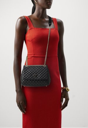 Femme portant une robe sans manches rouge et un sac bandoulière noir matelassé avec une chaîne dorée.