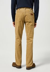 Pantaloni in corduroy color sabbia con design a gamba dritta, dotati di due tasche posteriori e una superficie testurizzata. Etichetta in pelle sul cinturino.