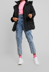 Svart vadderad jacka med hög krage, rosa toppen, ljusblå högmidjade jeans och vita sneakers med rosa strumpor.