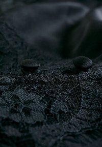 Schwarzer Spitzenstoff mit komplizierten Blumenmustern, ergänzt durch zwei runde schwarze Knöpfe, die strukturierte Details zeigen.