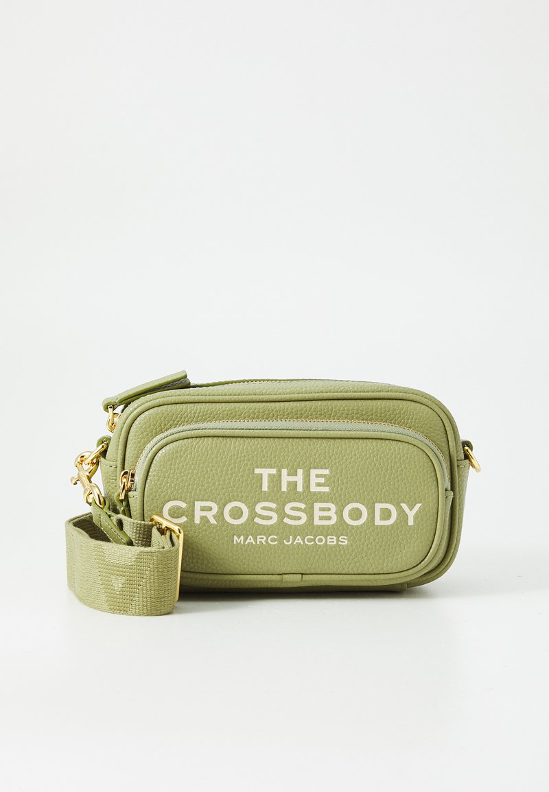 Olivově zelená crossbody taška s texturovanou kůží, dvěma zipovými přihrádkami, zlatými kovovými doplňky a tiskem bílé textu "THE CROSSBODY MARC JACOBS."