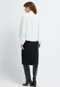 Hvidt langærmet bluse med pufærmer; sat sammen med en sort knælang blyantskirt og skinnende, knæhøje sorte støvler.