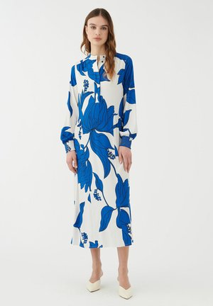 Abito a maniche lunghe bianco con grande motivo floreale blu. Presenta un colletto alto e maniche arricciate, completate da polsini blu testurizzati.