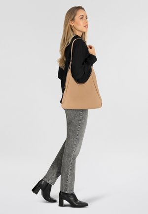 Borsa a spalla beige con texture liscia e leggero lucido, caratterizzata da una sola tracolla e forma trapezoidale, abbinata a jeans grigi e tacchi neri.