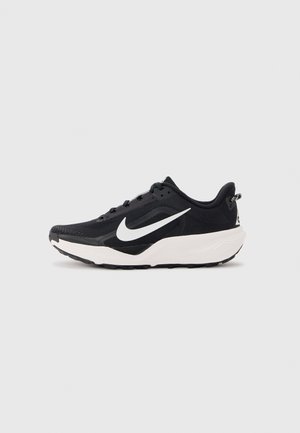 Zapatilla de correr Nike en blanco y negro con parte superior de malla, suela blanca y prominente logo Nike blanco en forma de ala en el lateral, vista desde el lado exterior.