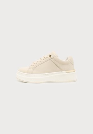 Beige lavtop sneaker med tyk hvid sål, snørelukning foran og polstret krave med tekstureret mønster på hælområdet.
