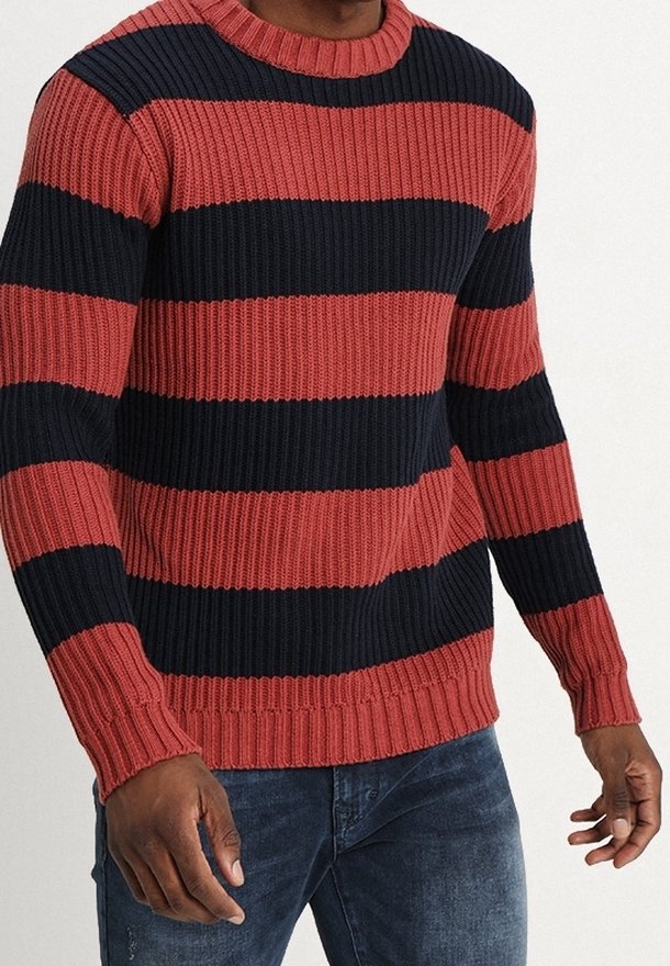 Knitted sweater with red and navy horizontal stripes, crew neck, ribbed texture, and cuffs. Worn over dark jeans.
