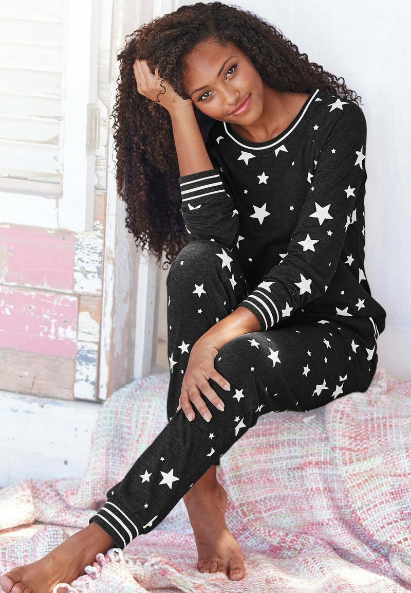 Black pajama set with white star patterns, featuring striped cuffs. Soft fabric, relaxed fit, full sleeves, and elastic ankle cuffs.