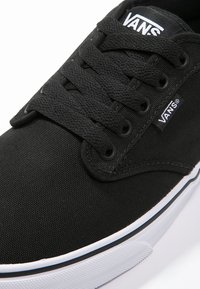 Sneaker nera in tela con design lace-up, occhielli rotondi e suola in gomma bianca con una linea di accento blu. Logo VANS sulla linguetta.