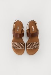 Brown leather sandals with a woven patterned strap and an adjustable ankle buckle, featuring a flat sole and soft interior lining.