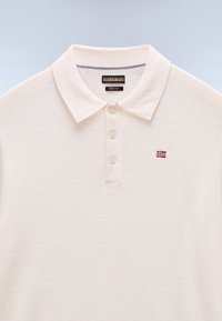Kreemi värvi meriinovillane polo särk klassikalise krae, kolme nupuga ja väikese tikitud Norra lipu detailiga.