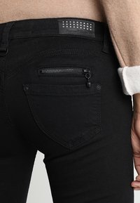 Svarta jeans med en texturerad midjeband som har rhinestones, en liten ficka med dragkedja bak och standard sömdetaljer.