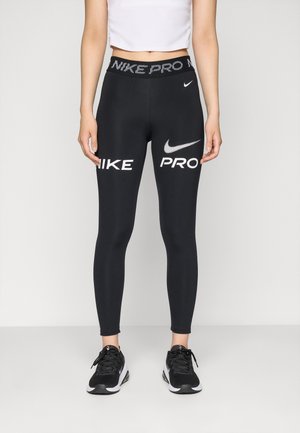 Black Nike Pro leggings with white logo and text accents. High waistband, smooth fabric, fitted shape, paired with black athletic shoes.